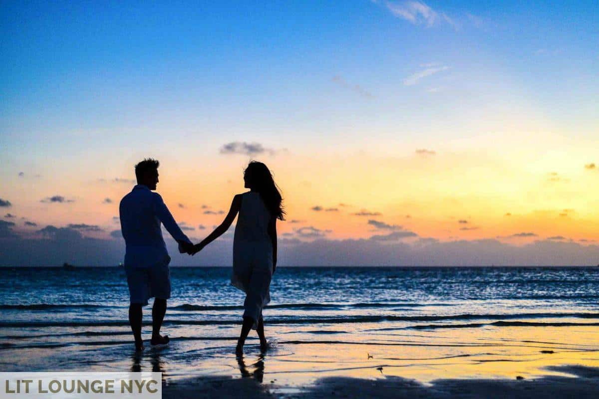 Man and Woman Holding Hands Walking on Seashore during Sunrise